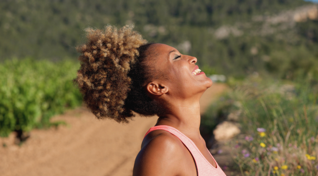 Woman enjoying sunlight outdoors, eyes closed, representing relaxation and body awareness in spring