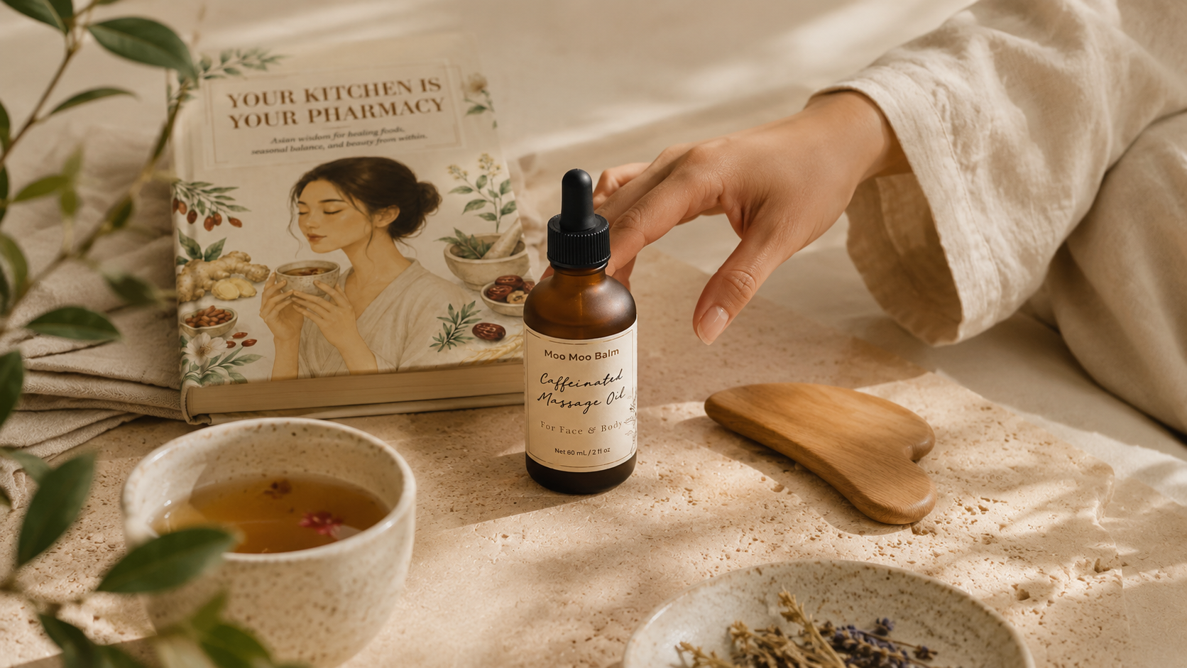 Moo Moo Balm ritual setup featuring the Caffeinated Massage Oil, wooden gua sha tool, herbal tea, and “Your Kitchen Is Your Pharmacy” ebook in soft morning light. A calming skincare and wellness scene inspired by Asian skincare wisdom, facial massage, and nervous system rituals.