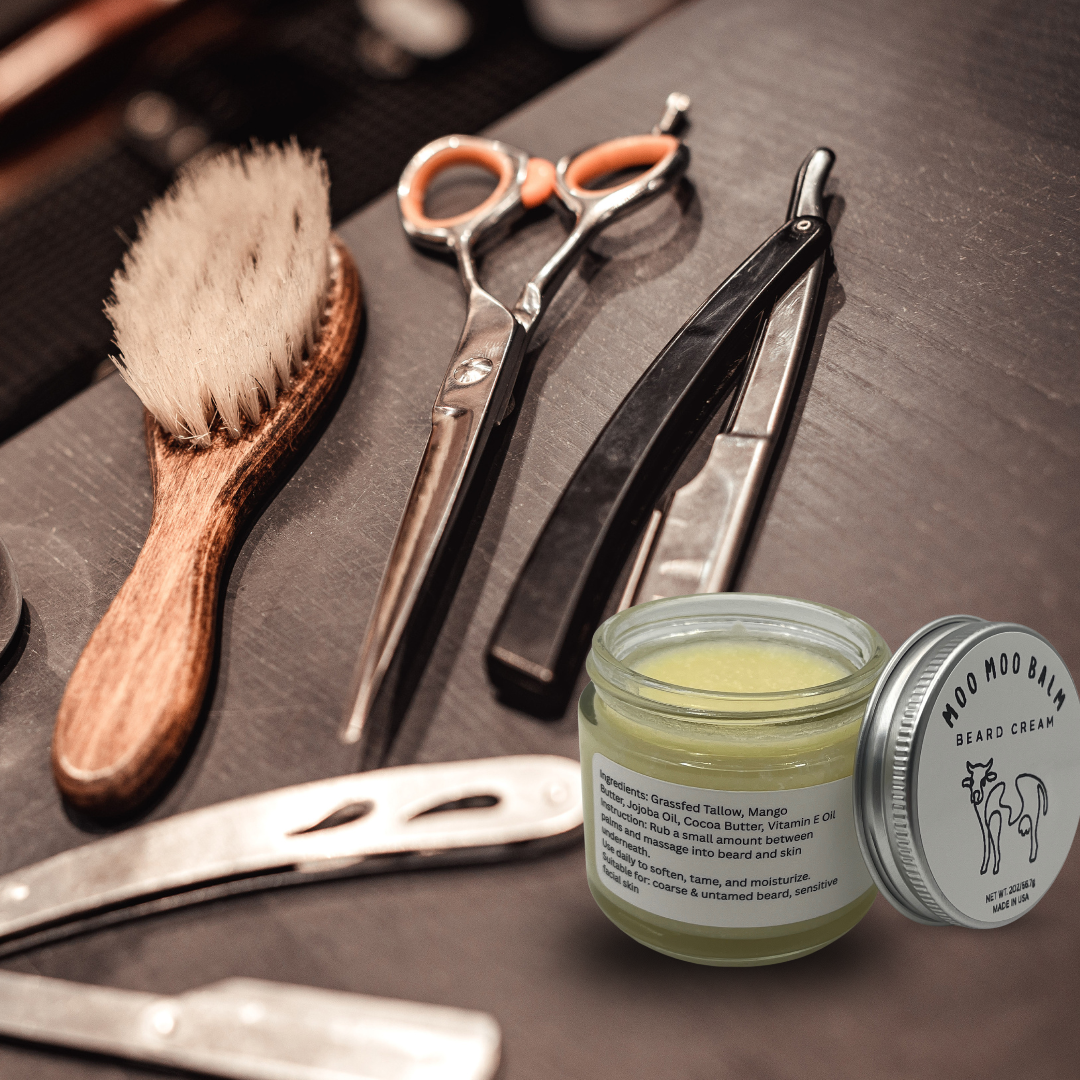 Moo Moo Balm Moostache Beard Cream jar placed beside barber tools and grooming brush, handcrafted with grass-fed tallow and cocoa butter for softening, moisturizing, and taming coarse beards.