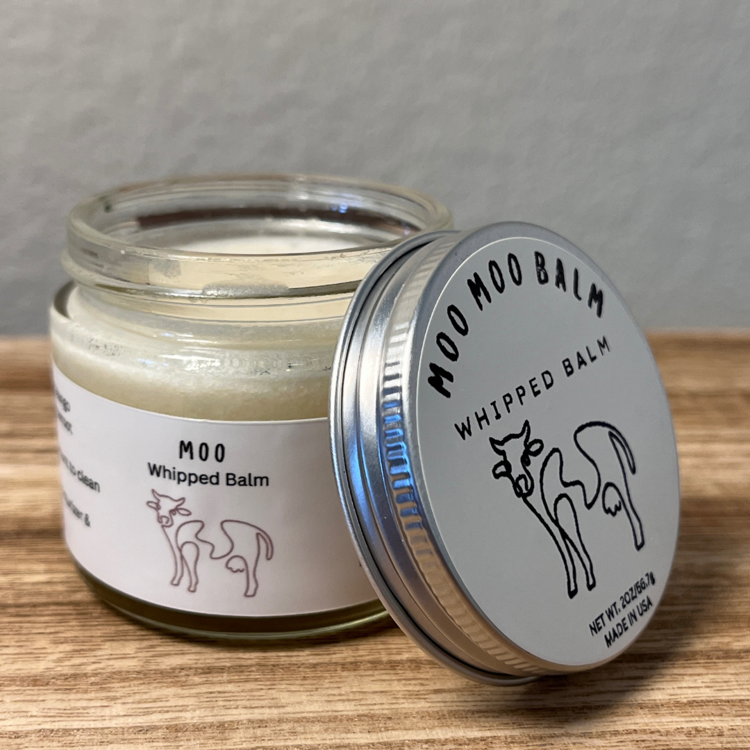 Open jar of Moo Moo Balm whipped tallow moisturizer on wooden surface, handcrafted from grass-fed tallow for deep hydration and skin repair.