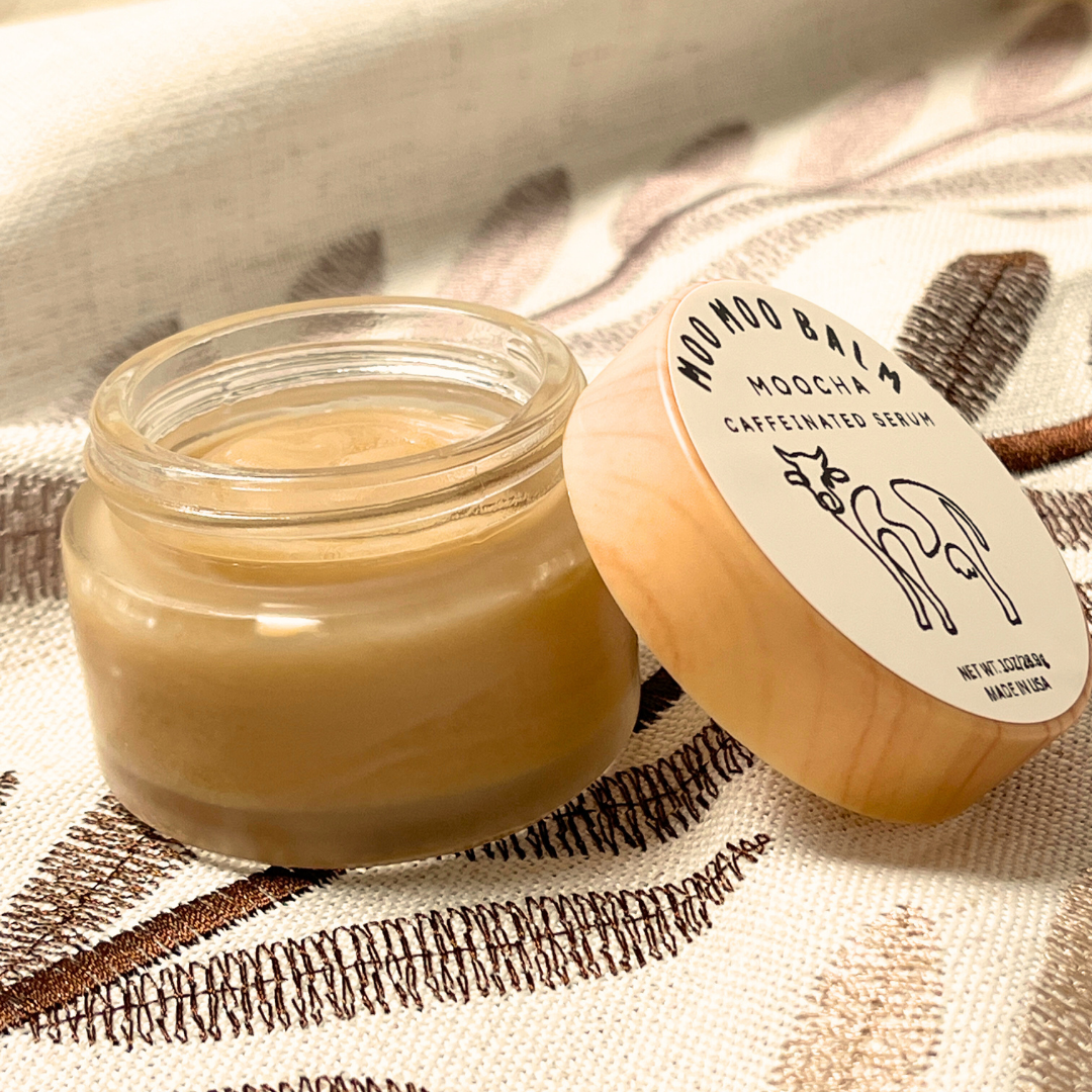 Moo Moo Balm Moocha Caffeinated Serum in an open glass jar with wooden lid, shown on a soft fabric background — natural tallow-based eye and face moisturizer enriched with coffee and vitamin E.